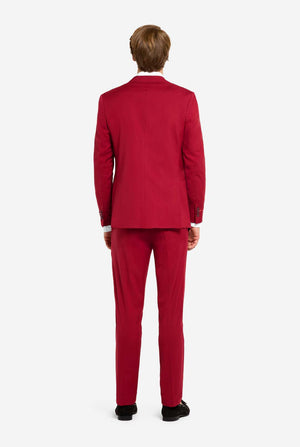 Afbeelding met lichtgrijze achtergrond en man die helder bordeauxrood mannenpak en wit overhemd draagt. Kostuum bestaat uit blazer en broek. Zicht vanaf de achterkant.