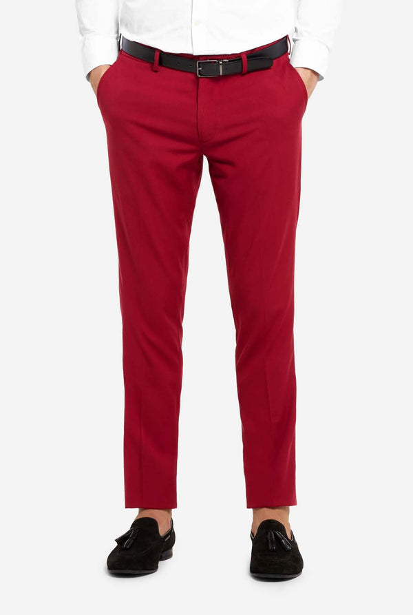 Afbeelding met lichtgrijze achtergrond en man die helder bordeauxrood mannenpak en wit overhemd draagt. Kostuum bestaat uit blazer en broek. Gericht op de broek.