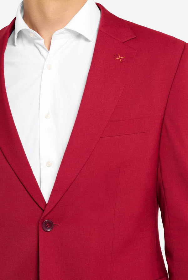 Afbeelding met lichtgrijze achtergrond en man die helder bordeauxrood mannenpak en wit overhemd draagt. Kostuum bestaat uit blazer en broek. Gericht op de borst.