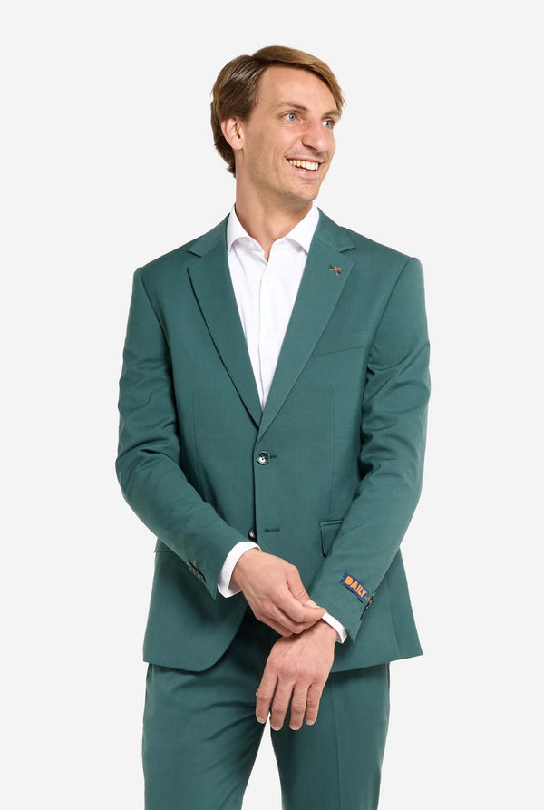 Afbeelding met lichtgrijze achtergrond en een man in een donkergroen herenpak en wit overhemd. Het pak bestaat uit een blazer en een pantalon. De man kijkt zijwaarts.