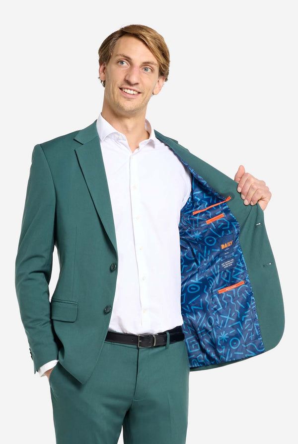 Afbeelding met lichtgrijze achtergrond en een man in een donkergroen herenpak en wit overhemd. Het pak bestaat uit een blazer en een pantalon. De man kijkt zijwaarts.