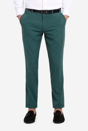 Afbeelding met lichtgrijze achtergrond en een man in een donkergroen herenpak en wit overhemd. Het pak bestaat uit een blazer en een pantalon. Close up van de broek