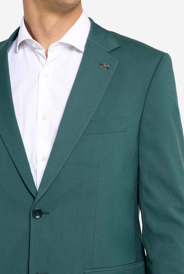 Afbeelding met lichtgrijze achtergrond en een man in een donkergroen herenpak en wit overhemd. Het pak bestaat uit een blazer en een pantalon. Close up van de borst