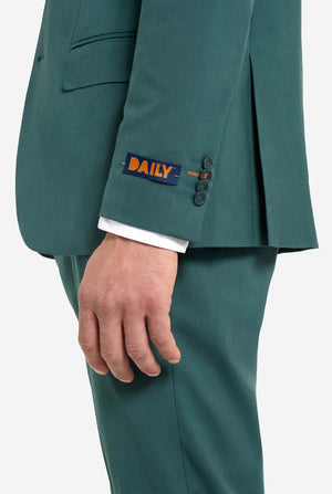Afbeelding met lichtgrijze achtergrond en een man in een donkergroen herenpak en wit overhemd. Het pak bestaat uit een blazer en een pantalon. Zicht vanaf de zijkant van de bovenkant van de broek en de onderkant van het jasje