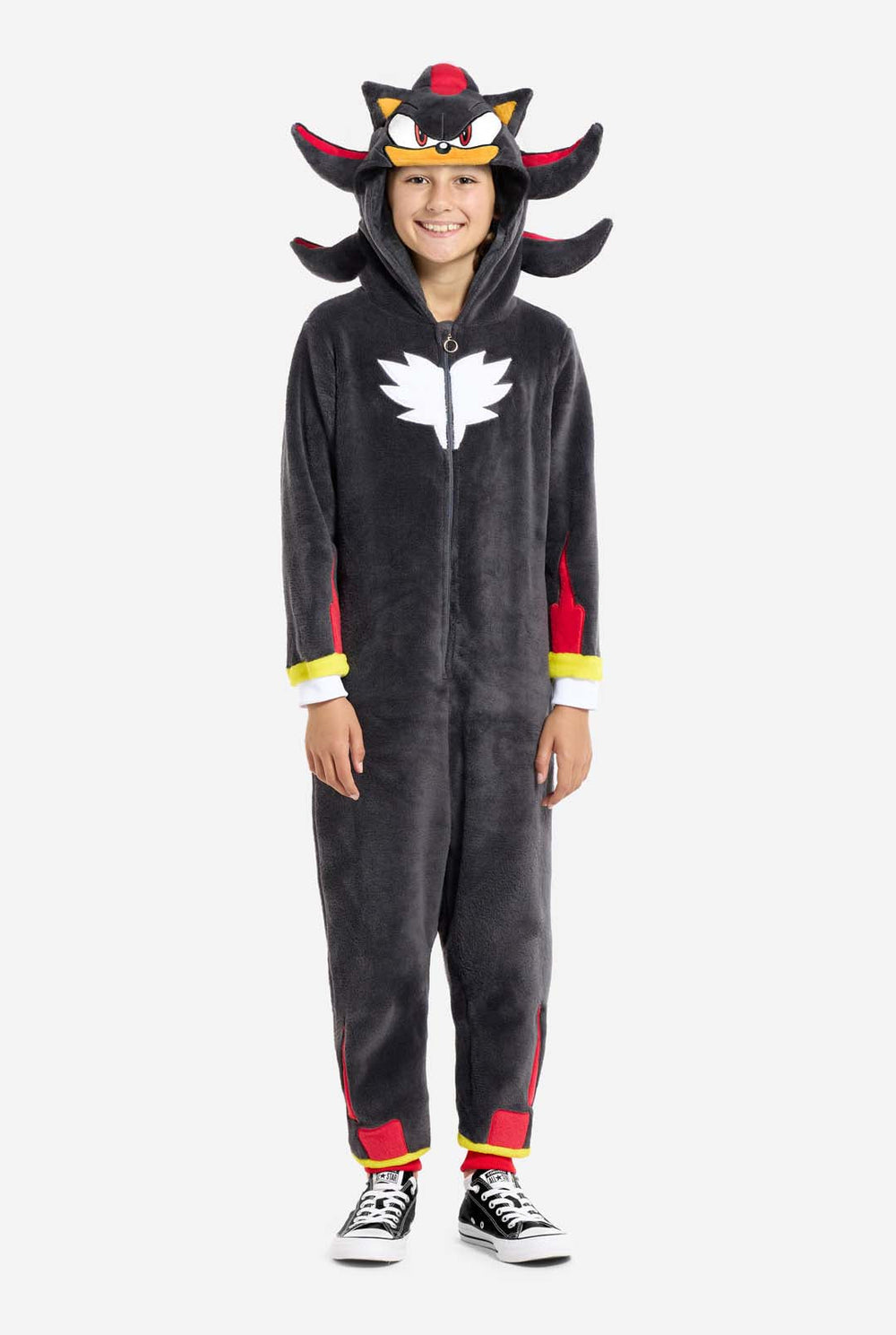 Een kind draagt ​​een pluchen, zwart kinderonesie, geïnspireerd op het populaire egelpersonage Shadow, met rode en zwarte accenten op de capuchon, een wit embleem op de borst en gele details op de polsen. De onesie is gemaakt van zacht fleecemateriaal en biedt comfort en een speels design voor cosplay, loungen of thema-evenementen. De persoon lacht met de capuchon op zijn hoofd. Perfect voor fans van games of animatiefiguren.