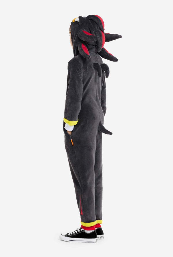 Een kind dat een pluchen zwarte kinderonesie draagt, geïnspireerd op het populaire egelkarakter Shadow, met stekelige rode en zwarte accenten op de capuchon, een wit embleem op de borst en gele polsdetails. De onesie is gemaakt van zacht fleecemateriaal en biedt comfort en een speels ontwerp voor cosplay, loungen of thema-evenementen. Zijaanzicht. Perfect voor fans van gaming of geanimeerde karakters.