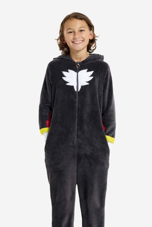 Een kind dat een pluchen zwarte kinderonesie draagt, geïnspireerd op het populaire egelkarakter Shadow, met stekelige rode en zwarte accenten op de capuchon, een wit embleem op de borst en gele polsdetails. De onesie is gemaakt van zacht fleecemateriaal en biedt comfort en een speels ontwerp voor cosplay, loungen of thema-evenementen. De persoon lacht terwijl de kap op de rug ligt. Perfect voor fans van gaming of geanimeerde karakters.
