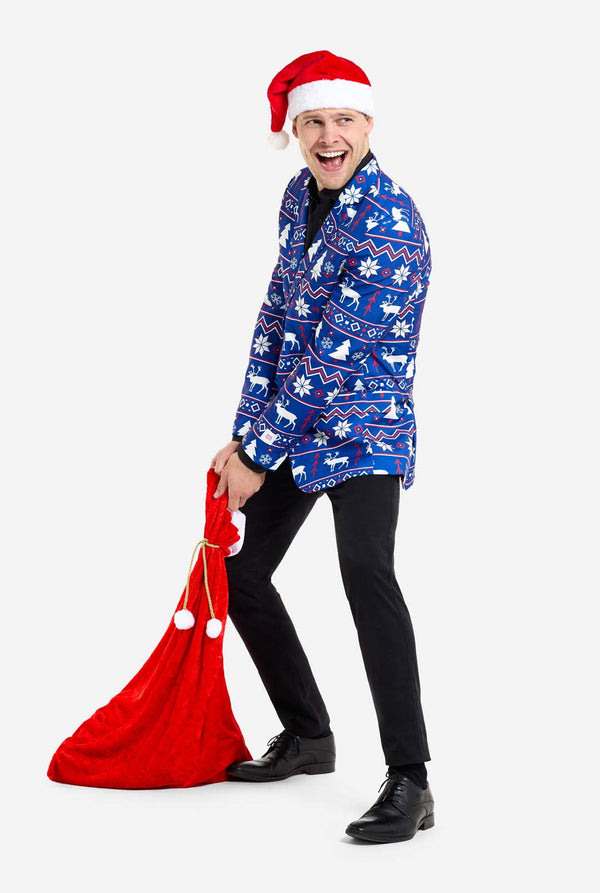 Man met blauwe kerstblazer voor mannen met Noordse kerstfiguren. Man draagt ​​ook een zwarte broek en een zwart herenoverhemd, een kerstmuts en een kersttas.