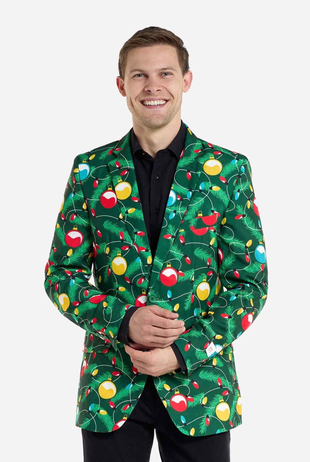Man met groene kerstblazer voor heren met versierde kerstboomprint. Man draagt ​​ook een zwarte broek en een zwart herenoverhemd.