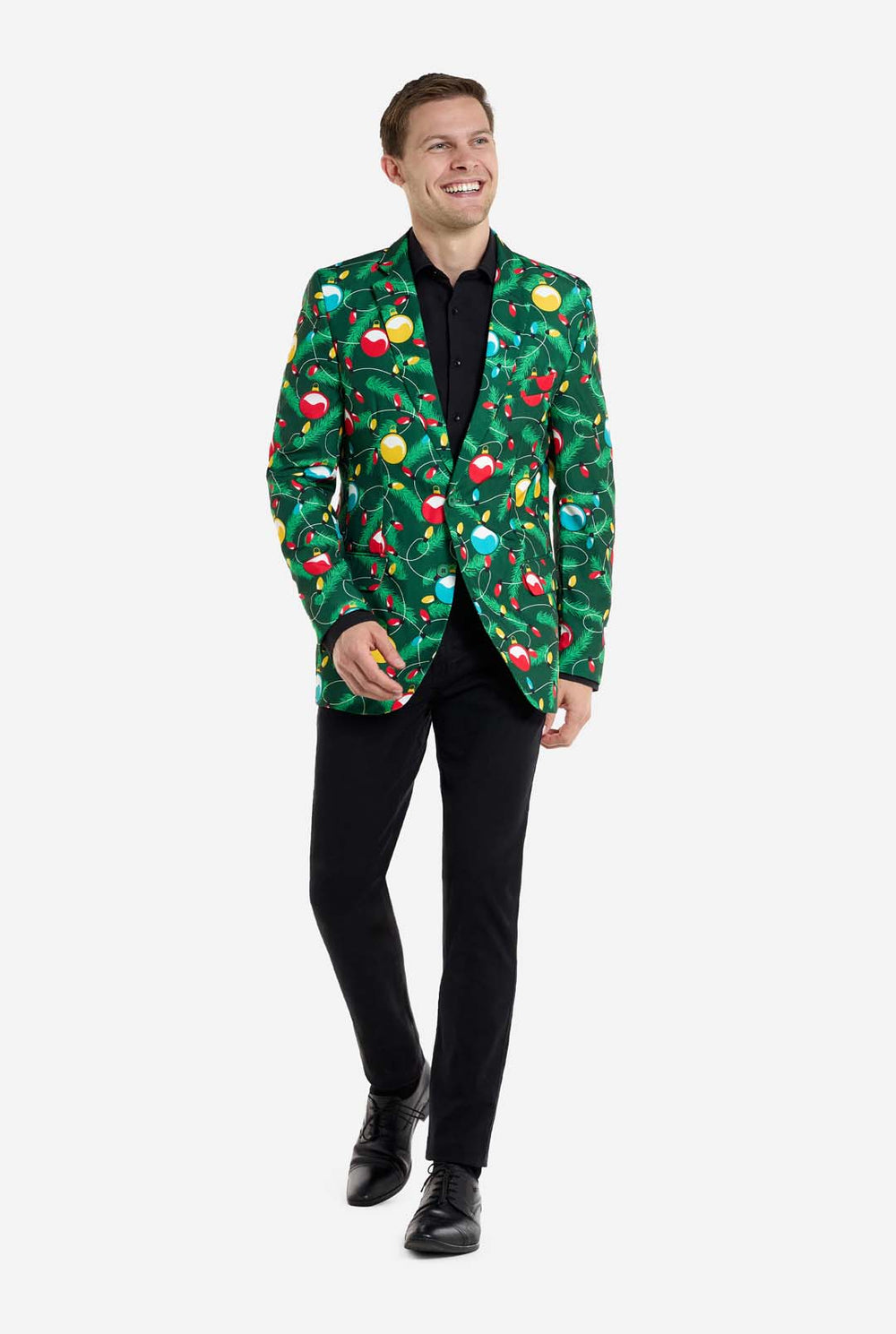 Man met groene kerstblazer voor heren met versierde kerstboomprint. Man draagt ​​ook een zwarte broek en een zwart herenoverhemd.