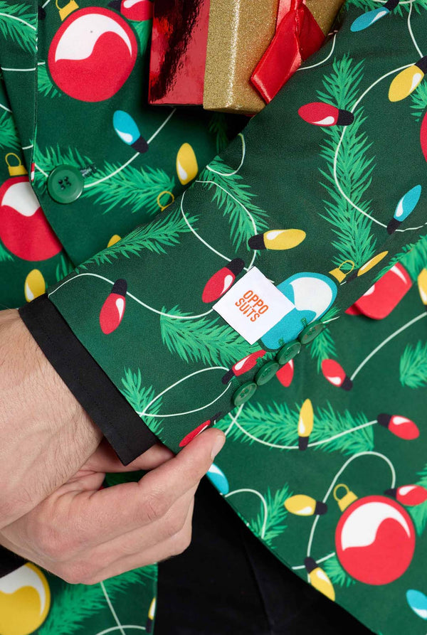 Man met groene kerstblazer voor heren met versierde kerstboomprint. Man draagt ​​ook een zwarte broek en een zwart herenoverhemd. Mouw close-up.