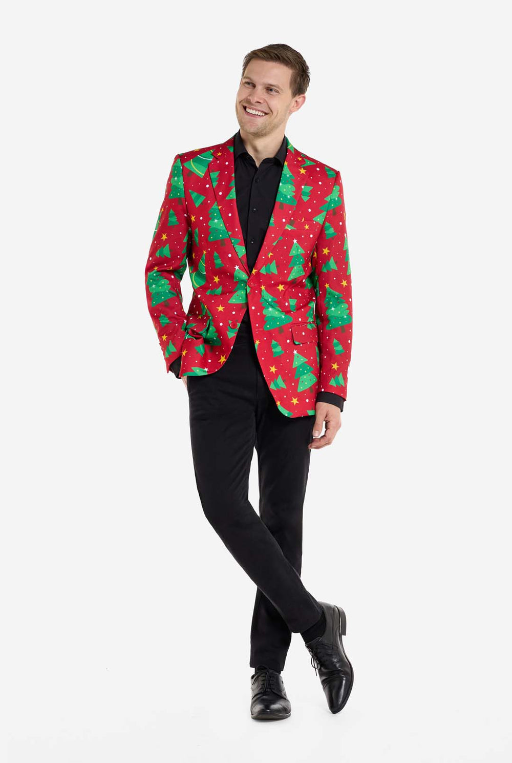 Man met rode kerstblazer voor heren met kerstbomen en sterrenprint. Man draagt ​​ook een zwarte broek en een zwart herenoverhemd.
