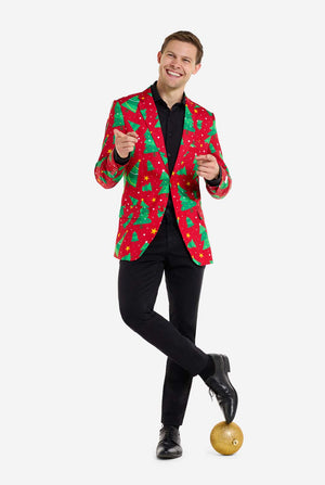 Man met rode kerstblazer voor heren met kerstbomen en sterrenprint. Man draagt ​​ook een zwarte broek en een zwart herenoverhemd. Staande met één voet op de kerstbal. Volledig lichaamsbeeld.