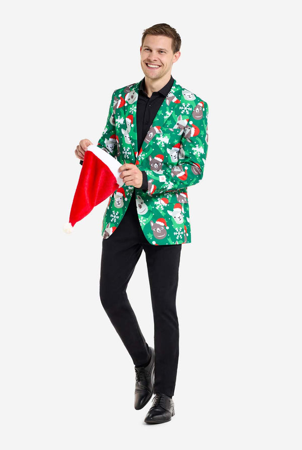 Man met groene kerstblazer voor mannen met kerstlama's. Man draagt ​​ook een zwarte broek en een zwart herenoverhemd. Kerstmuts vasthouden.