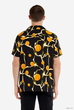 Man in zwart Hawaiiaans shirt met Dragon Ball Z-print, met Dragon Balls en bliksem. Hij draagt ​​ook een wit T-shirt en een zwarte broek. Beeld van de achterkant