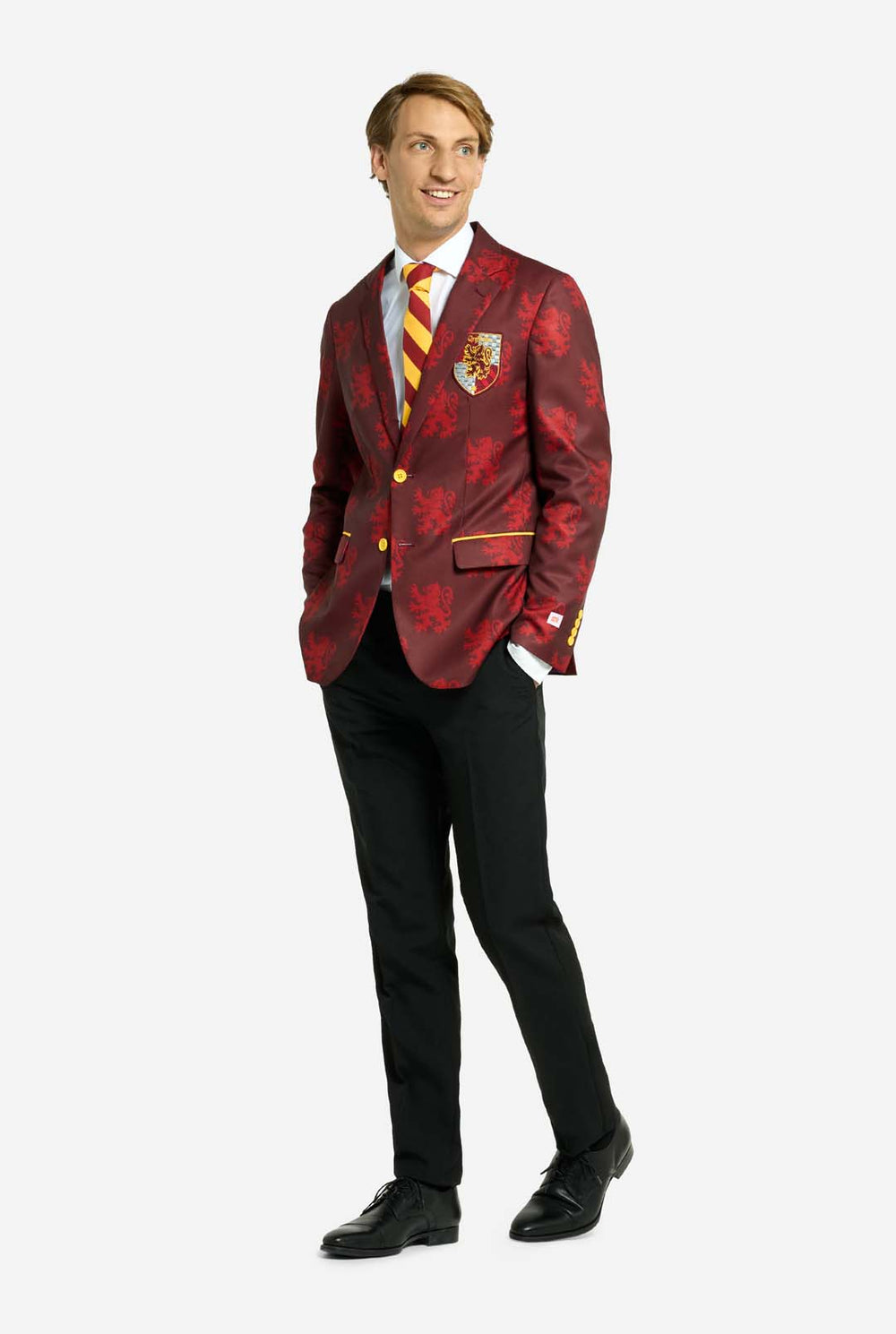 Afbeelding met lichtgrijze achtergrond en man in Harry Potter-pak, in Griffoendor-stijl. Het pak bestaat uit een rode blazer met Griffoendor-logo en lichtrode leeuwenprint, een zwarte broek en een rood-gele diagonaal gestreepte stropdas.