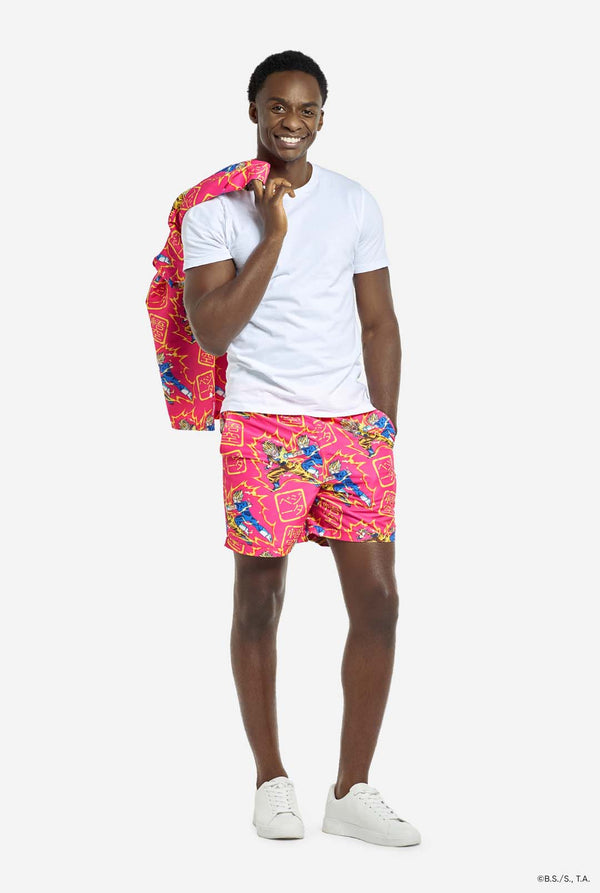 Man draagt ​​roze zomerset bestaande uit shirt en shorts. De zomerset heeft een Dragon Ball Z vechtende Goku en Vegeta print. Draagt shirt over zijn schouder en heeft een wit t-shirt aan.