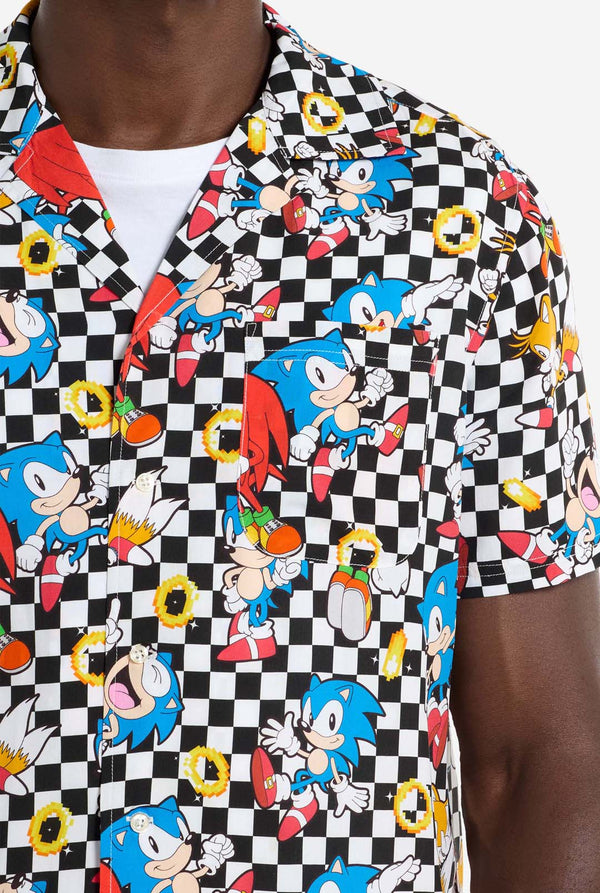 Een man draagt ​​een zwart-wit geruit Hawaï-shirt met personages uit de Sonic the Hedgehog-franchise en gouden ringen erop. Close up van de borst