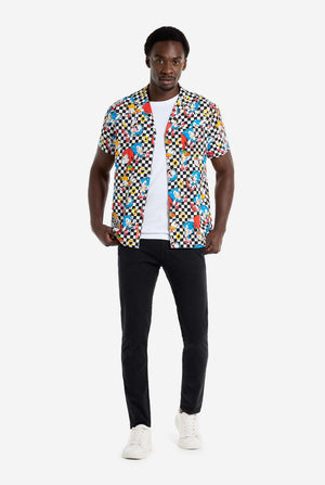 Een man draagt ​​een zwart-wit geruit Hawaï-shirt met personages uit de Sonic the Hedgehog-franchise en gouden ringen erop. Draag ook een zwarte broek. Hij kijkt in de camera en houdt de onderkant van het shirt vast.
