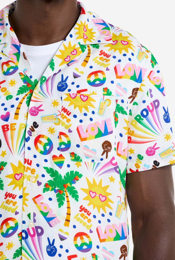 Foto van ​​een wit Hawaiiaans shirt met een regenboogprint. De print bestaat uit vredessymbolen, hartjes en andere iconen. 