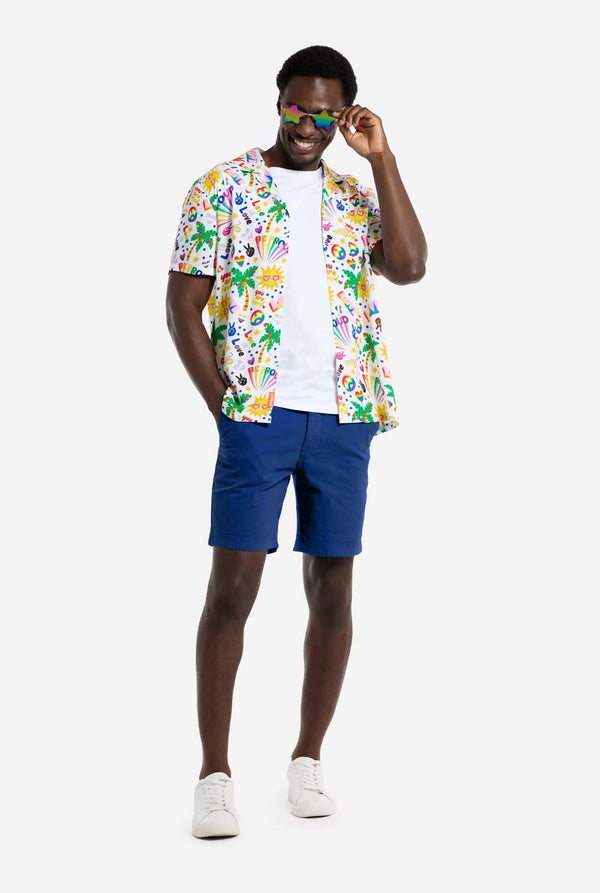 Een man draagt ​​een wit Hawaiiaans shirt met een regenboogprint. De print bestaat uit vredessymbolen, hartjes en andere iconen. Hij draagt ​​ook een blauwe broek.