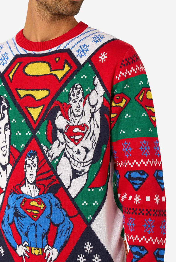 Man in een kleurrijke gebreide kersttrui met verschillende Superman-prints en het iconische “S”-logo.