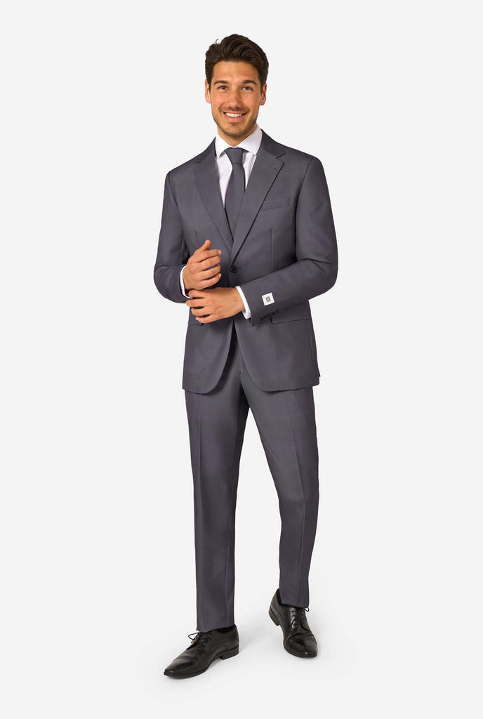 Een man draagt ​​een stijlvol antracietgrijs pak met een wit overhemd en ziet er zelfverzekerd uit. Perfecte formele outfit voor speciale gelegenheden, bruiloften en feesten. Volledig beeld.