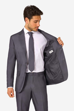 Een man draagt ​​een stijlvol antracietgrijs pak met een wit overhemd en ziet er zelfverzekerd uit. Perfecte formele outfit voor speciale gelegenheden, bruiloften en feesten. 1 kant van jasje open.
