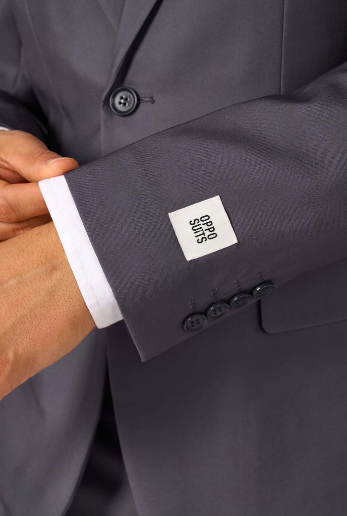 Een man draagt ​​een stijlvol antracietgrijs pak met een wit overhemd en ziet er zelfverzekerd uit. Perfecte formele outfit voor speciale gelegenheden, bruiloften en feesten. Close-up mouw.
