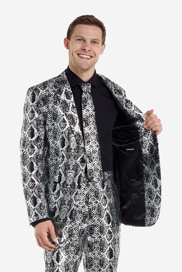 Een man draagt ​​een opvallend zilver-zwart pak met slangenprint van OppoSuits. Het opvallende pak heeft een opvallend slangenpatroon en biedt een strakke, modieuze look, perfect voor feestjes, evenementen of voor het maken van een gedurfd modestatement. Het herenpak wordt gecombineerd met een zwart overhemd en een bijpassende stropdas met slangenprint, wat een verfijnd tintje toevoegt aan het geheel. De man houdt de zijkant van de jas open.