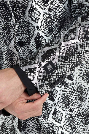 Een man draagt ​​een opvallend zilver-zwart pak met slangenprint van OppoSuits. Het opvallende pak heeft een opvallend slangenpatroon en biedt een strakke, modieuze look, perfect voor feestjes, evenementen of voor het maken van een gedurfd modestatement. Het herenpak wordt gecombineerd met een zwart overhemd en een bijpassende stropdas met slangenprint, wat een verfijnd tintje toevoegt aan het geheel. Close-up van de mouw.
