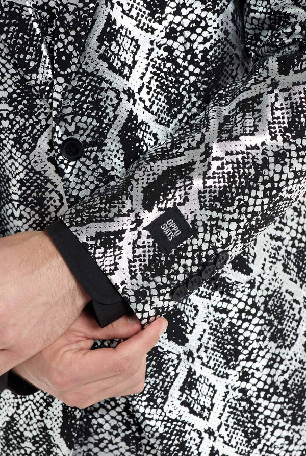 Een man draagt ​​een opvallend zilver-zwart pak met slangenprint van OppoSuits. Het opvallende pak heeft een opvallend slangenpatroon en biedt een strakke, modieuze look, perfect voor feestjes, evenementen of voor het maken van een gedurfd modestatement. Het herenpak wordt gecombineerd met een zwart overhemd en een bijpassende stropdas met slangenprint, wat een verfijnd tintje toevoegt aan het geheel. Close-up van de mouw.