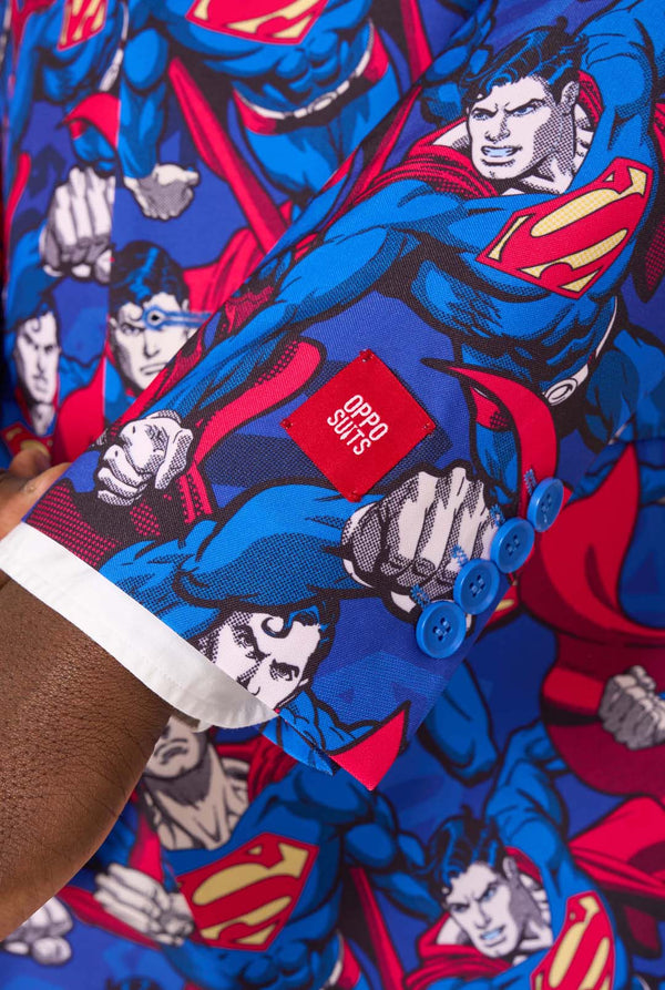 Een man draagt een pak met Superman-thema, een rode stropdas en een wit overhemd op een witte achtergrond. Close up van de mouwen