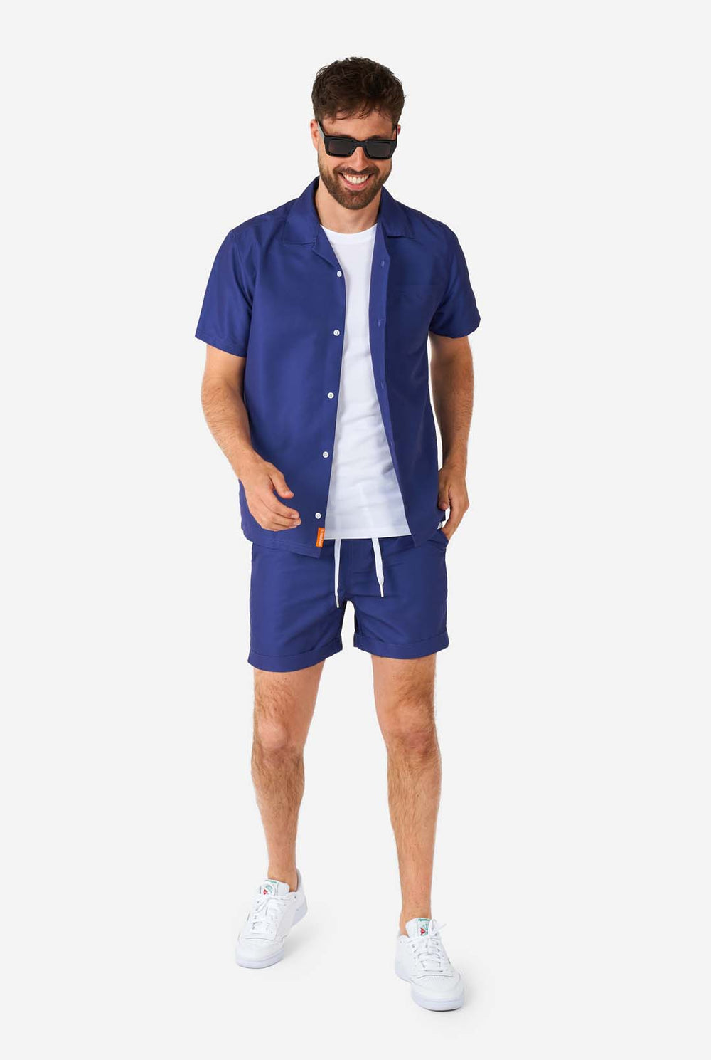 Man met blauwe zomerset bestaande uit shirt en korte broek en zonnebril.