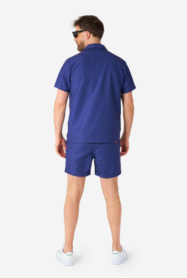 Man met blauwe zomerset bestaande uit shirt en korte broek, volledig lichaamsbeeld vanaf de achterkant