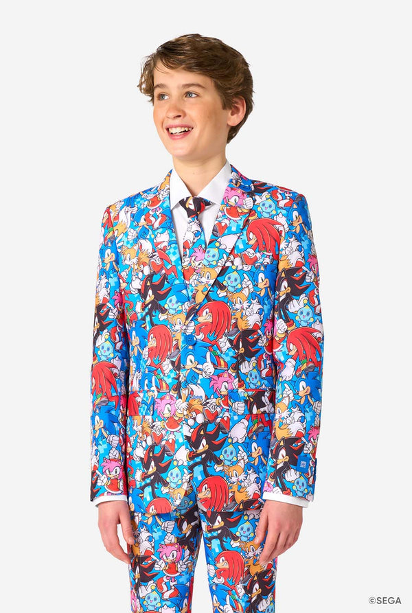 Tienerjongen draagt ​​een opvallend Sonic-tienerpak met kleurrijke prints van Sonic the Hedgehog-personages, waaronder Sonic, Knuckles, Tails en Amy, gecombineerd met een bijpassende stropdas en een wit overhemd.