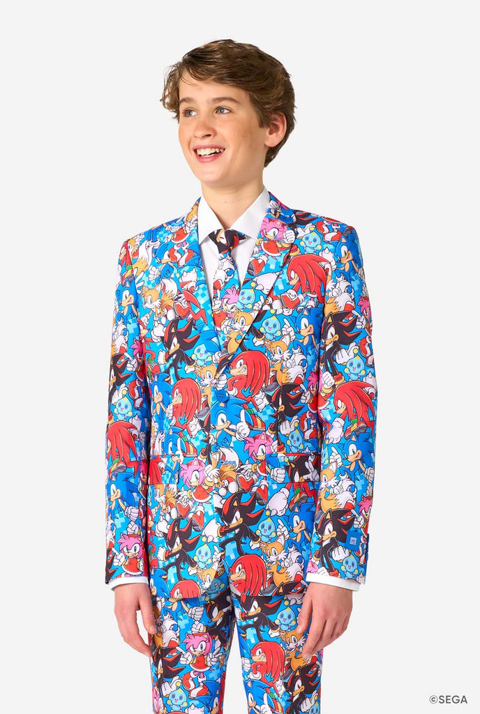 Tienerjongen draagt ​​een opvallend Sonic-tienerpak met kleurrijke prints van Sonic the Hedgehog-personages, waaronder Sonic, Knuckles, Tails en Amy, gecombineerd met een bijpassende stropdas en een wit overhemd.