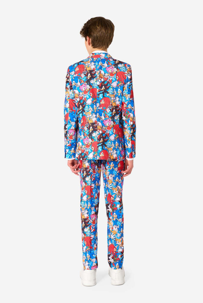 Tienerjongen draagt ​​een opvallend Sonic-tienerpak met kleurrijke prints van Sonic the Hedgehog-personages, waaronder Sonic, Knuckles, Tails en Amy, gecombineerd met een bijpassende stropdas en een wit overhemd. Gezien vanaf de achterkant.