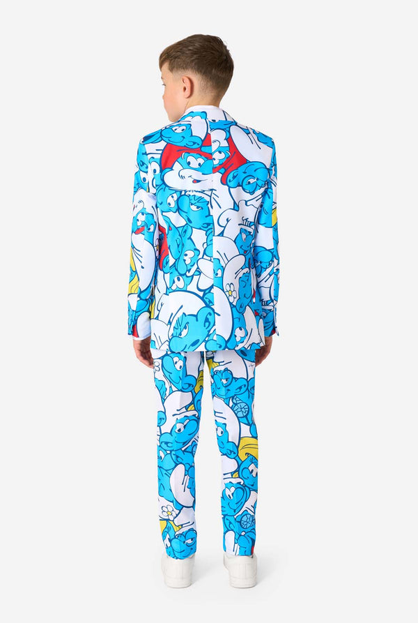 Een tienerjongen draagt ​​een opvallend Smurfenpak met kleurrijke cartoonfiguurprints in de kleuren blauw, rood, geel en wit, gecombineerd met een bijpassende stropdas en een wit overhemd, lachend tegen een effen achtergrond. Gezien vanaf de achterkant.