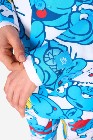 Een tienerjongen draagt ​​een opvallend Smurfenpak met kleurrijke cartoonfiguurprints in de kleuren blauw, rood, geel en wit, gecombineerd met een bijpassende stropdas en een wit overhemd, lachend tegen een effen achtergrond. Close up van de mouwen.