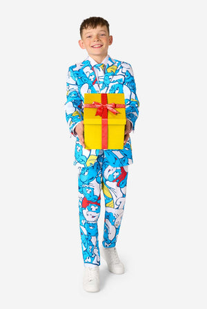 Een tienerjongen draagt ​​een opvallend Smurfenpak met kleurrijke cartoonfiguurprints in de kleuren blauw, rood, geel en wit, gecombineerd met een bijpassende stropdas en een wit overhemd, lachend tegen een effen achtergrond. Houd een cadeautje vast.