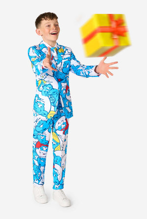 Een tienerjongen draagt ​​een opvallend Smurfenpak met kleurrijke cartoonfiguurprints in de kleuren blauw, rood, geel en wit, gecombineerd met een bijpassende stropdas en een wit overhemd, lachend tegen een effen achtergrond. Gooit een cadeautje.