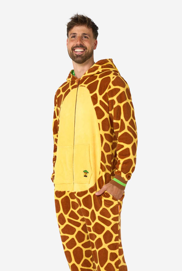Een lachende man draagt een bruine en gele onesie voor volwassenen die is ontworpen als een giraffe. De onesie heeft een capuchon die op een giraffekop lijkt en giraffedetails, perfect voor gezellig loungen of verkleedfeestjes. De man staat met zijn handen in de zakken.