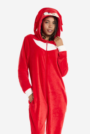 Een vrouw draagt ​​een felrode Knuckles the Echidna onesie voor volwassenen, een gezellige en speelse outfit geïnspireerd op het beroemde personage uit de Sonic the Hedgehog-serie. De onesie is voorzien van de kenmerkende witte borstpatch van Knuckles en heeft een capuchon die het gezicht van Knuckles laat zien, compleet met zijn expressieve ogen en lange rode dreads. De ritssluiting aan de voorkant zorgt voor gemakkelijk dragen.