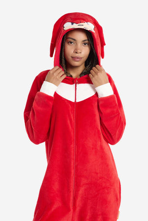 Een vrouw draagt ​​een felrode Knuckles the Echidna onesie voor volwassenen, een gezellige en speelse outfit geïnspireerd op het beroemde personage uit de Sonic the Hedgehog-serie. De onesie is voorzien van de kenmerkende witte borstpatch van Knuckles en heeft een capuchon die het gezicht van Knuckles laat zien, compleet met zijn expressieve ogen en lange rode dreads. De ritssluiting aan de voorkant zorgt voor gemakkelijk dragen, en heeft de capuchon op en houdt het vast.
