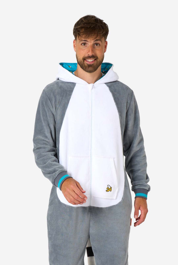 Een man draagt ​​een grijze en witte maki onesie voor volwassenen met speelse capuchondetails en gezellig, zacht materiaal, perfect voor loungen of verkleedevenementen. Inclusief zwart-witte staart. De capuchon hangt op zijn rug.