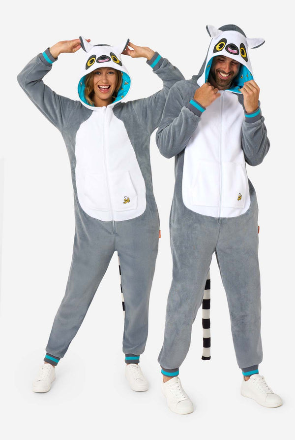 Een man en vrouw dragen een grijze en witte maki onesie voor volwassenen met speelse capuchondetails en knus, zacht materiaal, perfect om in te loungen of voor verkleedpartijen. Inclusief zwart-witte staart. De capuchon staat op hun hoofd. Volledig lichaam foto
