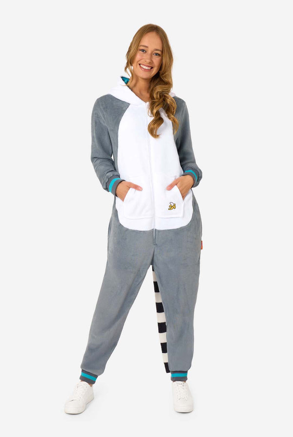 Een vrouw draagt een grijze en witte maki onesie voor volwassenen met speelse capuchondetails en knus, zacht materiaal, perfect om in te loungen of voor verkleedpartijen. Inclusief zwart-witte staart. De capuchon ligt op haar rug