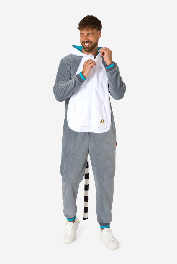 Een man draagt ​​een grijze en witte maki onesie voor volwassenen met speelse capuchondetails en gezellig, zacht materiaal, perfect voor loungen of verkleedevenementen. Inclusief zwart-witte staart. Volledig lichaamsbeeld met de kap op zijn rug en zichtbare staart.
