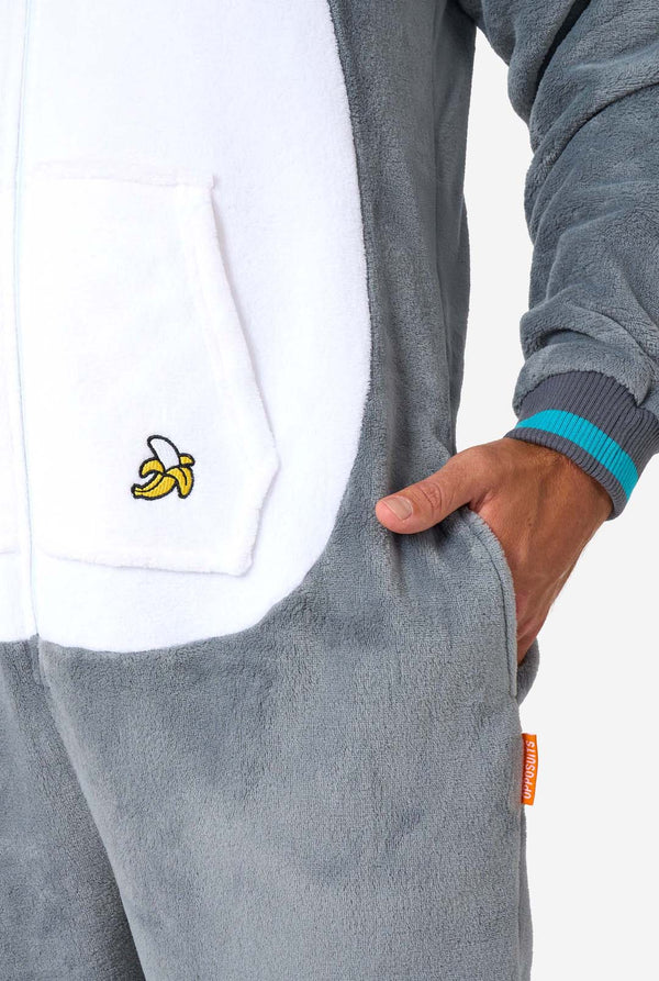 Een man draagt ​​een grijze en witte maki onesie voor volwassenen met speelse capuchondetails en gezellig, zacht materiaal, perfect voor loungen of verkleedevenementen. Inclusief zwart-witte staart. Zak close-up.